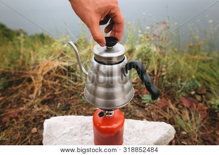 Steel Kettle Boiling On Gas Primus, Making Hot Drink At Picnic Outdoors. Brewing Coffee In The Morni
