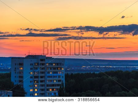 Building In The Town Outskirts At Dusk. House Separately Standing Among Trees Crowns. Lights In Wind