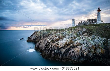 The ruins of the abbey of Saint-Mathieu de Fine-Terre and the lighthouse in the sunset, Finistere, Brittany, France
