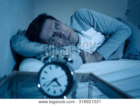 Portrait Of Young Man In Bed Staring At Alarm Clock Trying To Sleep Feeling Stressed And Sleepless