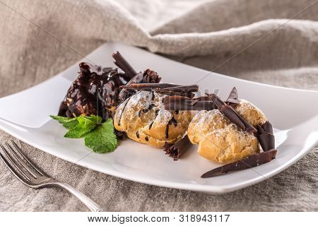 Homemade Profiteroles Dessert With Chocolate And Mint Leaf On White Plate On Grey Tablecloth Side Vi