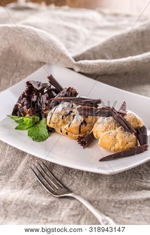 Homemade Profiteroles Dessert With Chocolate And Mint Leaf On White Plate On Grey Tablecloth Side Vi