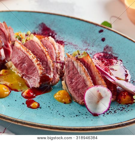 Macro shot of Sliced duck breast with hummus and plum sauce on turquoise plate. Exquisite serving restaurant main course with grilled goose fillet steak, greens and spices