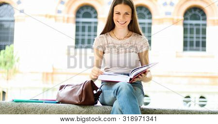 Beautiful female college student reading a book on a bench in a park
