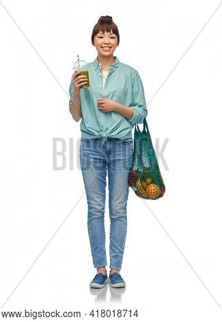 healthy eating and sustainability concept - asian woman drinking green smoothie from plastic cup and holding reusable string bag with fruits and vegetables over white background