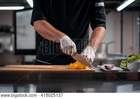 Close Up Of Chef Cook Hands In Gloves Cutting Or Chop Yellow Pepper At Kitchen