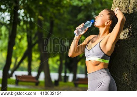Running Concepts. Portrait Of Sexy Caucasian Female Drinking Still Water During Exercises Near Tree