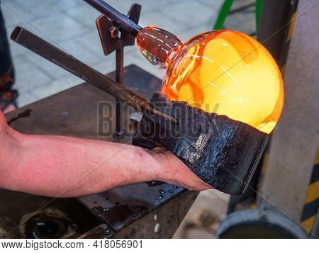 Glassblower Is Using Wet Wooden Form For Shaping The Red Melted Glass On The End Of Glassblowing Pip
