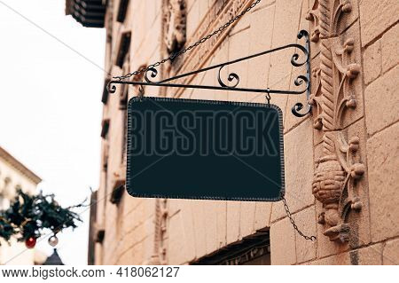 Stylish Rectangular Blank Sign In A Wrought-iron Frame Hangs On The Stone Wall Of An Ancient Buildin