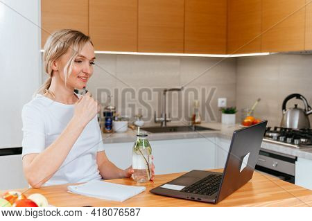 Blonde Girl With Laptop Drinking Majito Lemonade, Doing Homework In A Bright Kitchen. Education And 