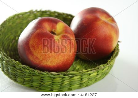 zwei rote Pfirsiche in einem grünen Korb