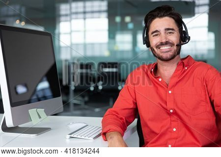 Portrait of caucasian businessman sitting at desk with blank screen wearing headset. independent creative design business.