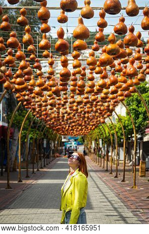 A Young Woman Tourist Walks Along A Pedestrian Street Decorated With A Suspension With Various Clay 