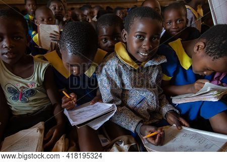 Mzuzu, Malawi. 30-05-2018. A Black Girl Is Looking At The Camera While Writing In Her Notebook As Th