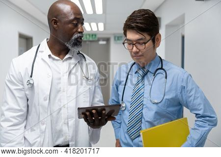 Couple of diverse male doctors walking through corridor looking at tablet. medicine, health and healthcare services.