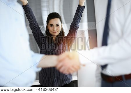 Happy And Excited Business Woman Raising Hands Because Of Success Agreement At Meeting. Two Men Shak