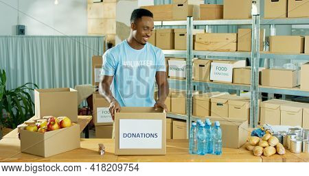 Happy African American Young Handsome Man Volunteer Smiling Working At Charity Center Giving Food To
