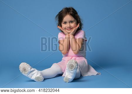 Portrait Of An Adorable Child Girl Ballerina Cute Smiling While Sitting On Blue Background With Spac