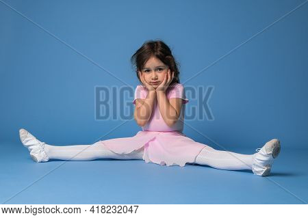 Cute Ballerina In Pink Dress Perfecting Twine While Sitting On Blue Background With Copy Space