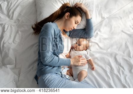 Tired Young Mother Sleping In Bed While Her Adorable Newborn Child Awake