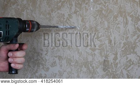 Husband Or Handyman Drills Hole In Marbled Painted Plaster Wall Surface. Male Hands Hold Electric Dr