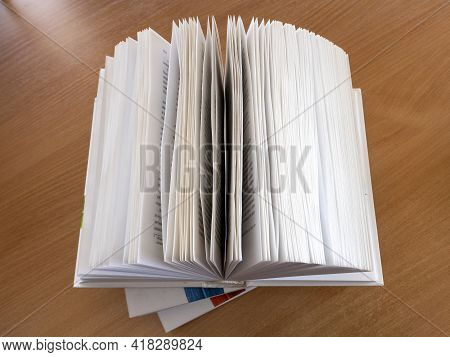 Top View Of A Hardback Book. The Books Are Stacked. The Top Volume Is Open, The Pages Are Fanned Out