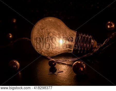 Close Up Of A Light Bulb Containing Tiny White Featers Laying On A Dark Surface Decorated With Golde