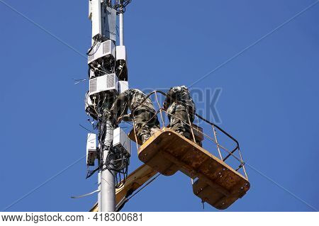 Installation Of Cellular Equipment On The Tower. Two Communications Engineers Work At Altitude From 