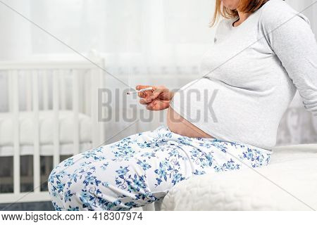 Pregnant Woman With A Cigarette In Her Hands, Sitting On The Bed. Hands With A Cigarette And Stomach