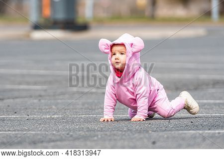 A Little Child In A Pink Dress Crawling On The Asphalt In A Car Parking Lot
