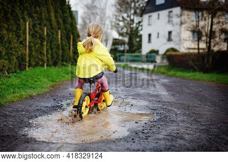 Little Toddler Girl Wearing Yellow Rain Gum Boots, Running With Balance Bike During Sleet. Happy Chi
