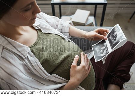 Pregnant Woman Sitting On Sofa And Resting She Looking At X-ray Image And Waiting For The Birth Of H