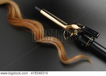 Professional Hairdressing Curling Iron With A lock Of CurlyHair On A Black Background, Spotted With Ray Of Lights