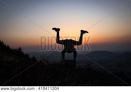 Silhouette Of Teenager And Athlete Trying A Handstand At Sunset In European Mountains. Training In N