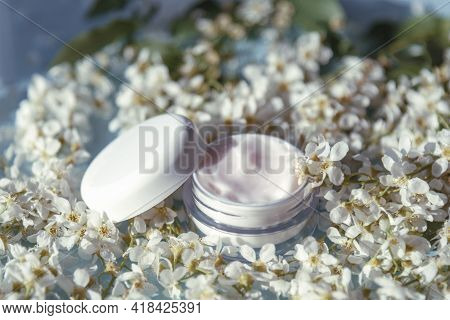 Cosmetic Cream Jar On The Background Of White Small Spring Flowers Of Byttneria. Natural Organic Cos