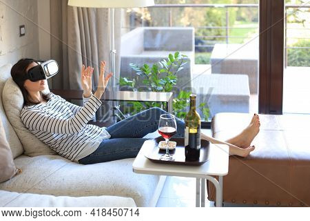 Young Casual Girl Wearing Vr Headset While Lounging On Couch At Home And Looking Around.