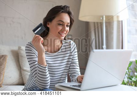 Happy Natural Brunette Using Credit Card And Laptop In The Living Room.
