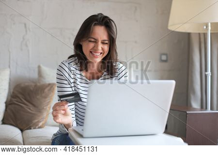 Happy Natural Brunette Using Credit Card And Laptop In The Living Room.