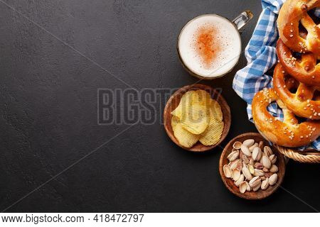 Lager beer mug, nuts, potato chips and fresh baked homemade pretzel with sea salt on stone table. Classic beer snack. Top view flat lay with copy space