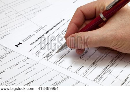 A Man Holding A Ballpoint Pen To Fill A Permanent Residence Visa Application Form To Canada.