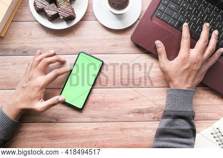 Top View Of Man Hand Using Smart Phone And Typing On Laptop