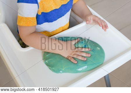 Child Play With Slime At Home In The Kitchen. Little Toddler Boy Squeeze And Stretching Green Slime 