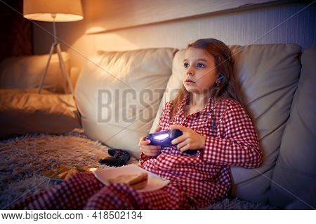 Happy Little Girl In Pajams Sitting On Sofa, Eating Pizza And Pl