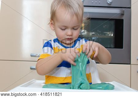 Child Play With Slime At Home In The Kitchen. Little Toddler Boy Squeeze And Stretching Green Slime