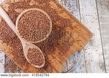 Scattered Buckwheat. Buckwheat In A Wooden Bowl And Spoon Lies On A Wooden Table. Scattered Buckwhea