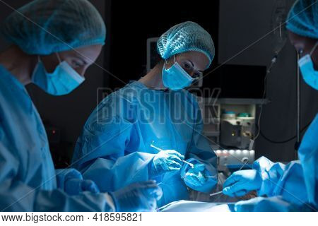 Diverse group of male and female surgeons in operating theatre wearing face masks performing surgery. medicine, health and healthcare services during coronavirus covid 19 pand