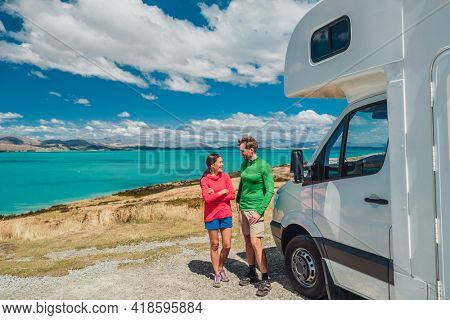 RV motorhome camper van road trip on New Zealand. Young couple on travel vacation adventure. Two tourists looking at Lake Pukaki and mountains on pit stop next to their rental car