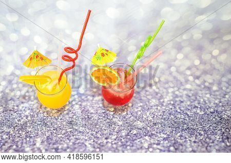 Two Glasses With Orange And Grapefruit Juice, With Ice And Straws Stand On A Gray Abstract Backgroun