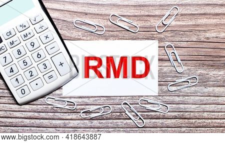 On A Wooden Background, A White Calculator, White Paper Clips And A White Card With The Text Rmd Req