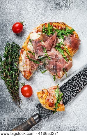 Italian Pizza With Parma Ham, Arugula And Cheeseon A Kitchen Table. White Background. Top View